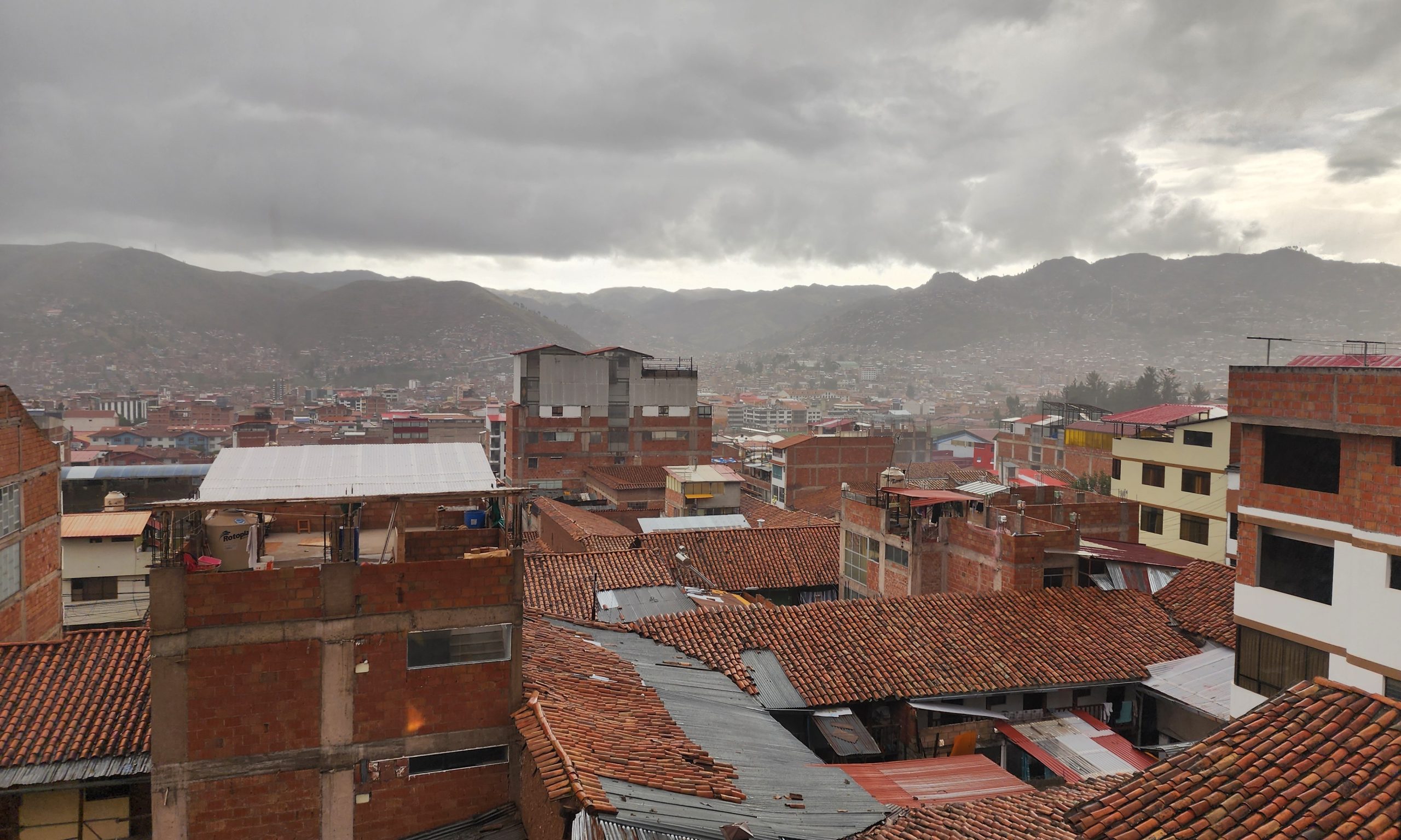 Cusco rooftops under overcast sky with terra cotta tile roofs receding into hazy Andean mountains