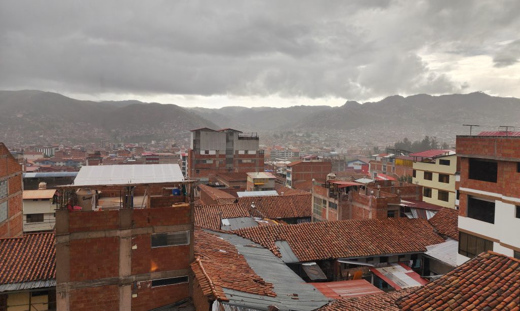 Cusco rooftops under overcast sky with terra cotta tile roofs receding into hazy Andean mountains