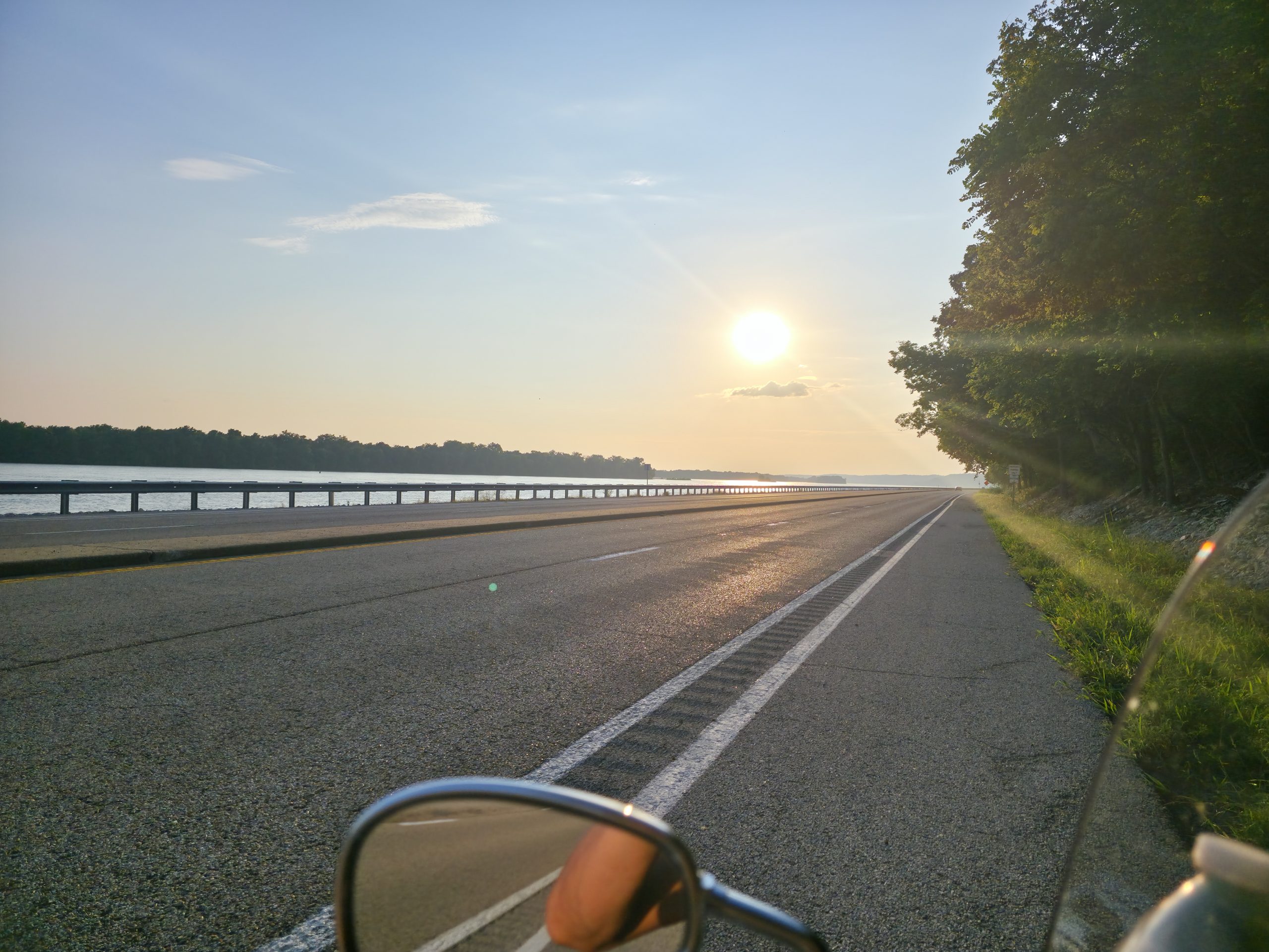 View of an open road from behind a motorcycle windshield with the sun in the sky