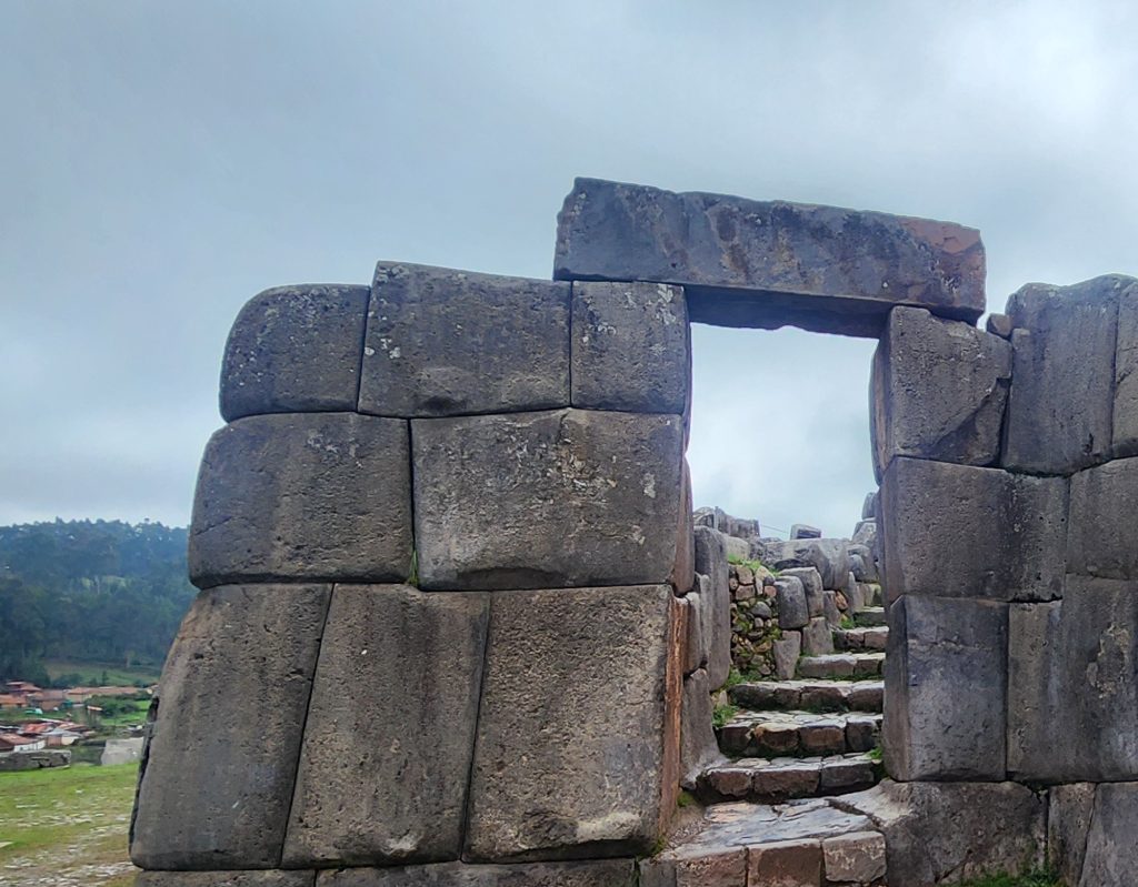 Trapezoidal Inca stone doorway with worn steps climbing up through it under an overcast Cusco sky