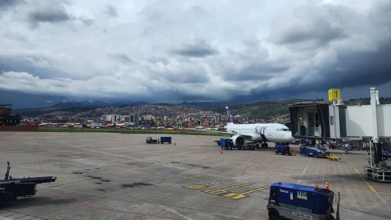 Jet parked at a Cusco airport gate under heavy gray overcast, Andes foothills behind the tarmac.
