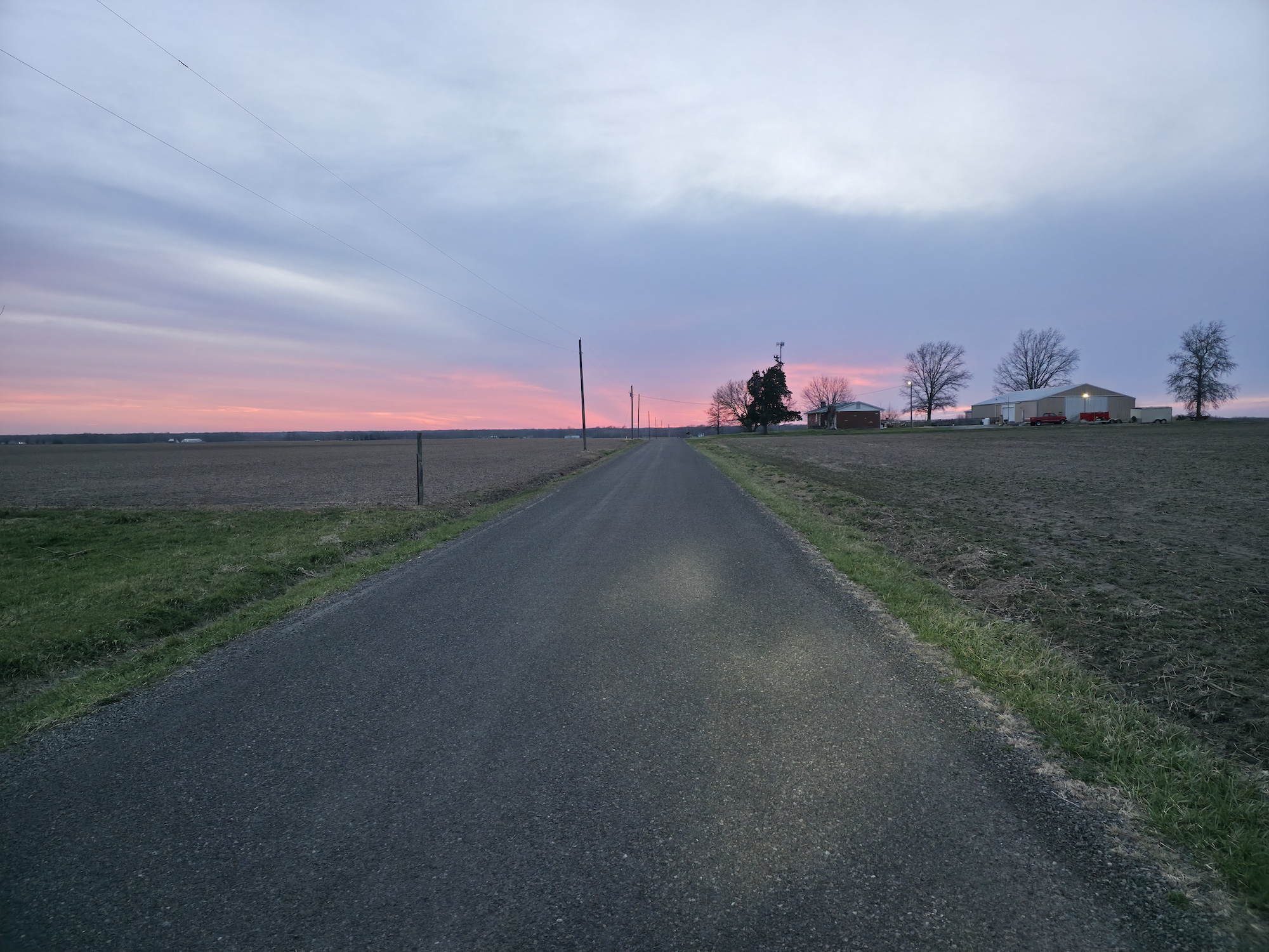 Empty country road running straight toward a pink dusk sky between flat, bare farm fields