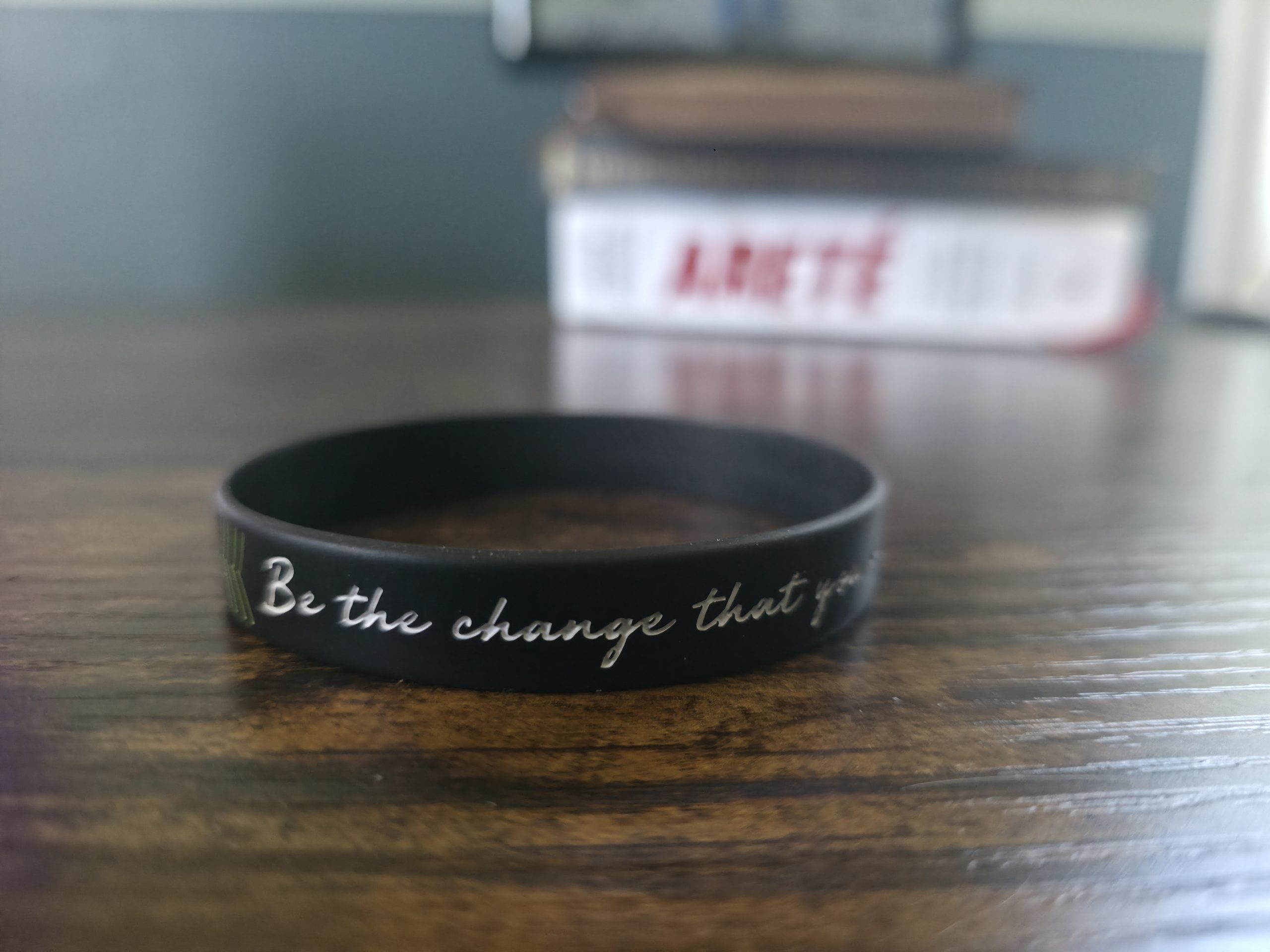 A worn silicone bracelet resting on a desk beside Brian Johnson's Areté, the lettering caught mid-fragment.