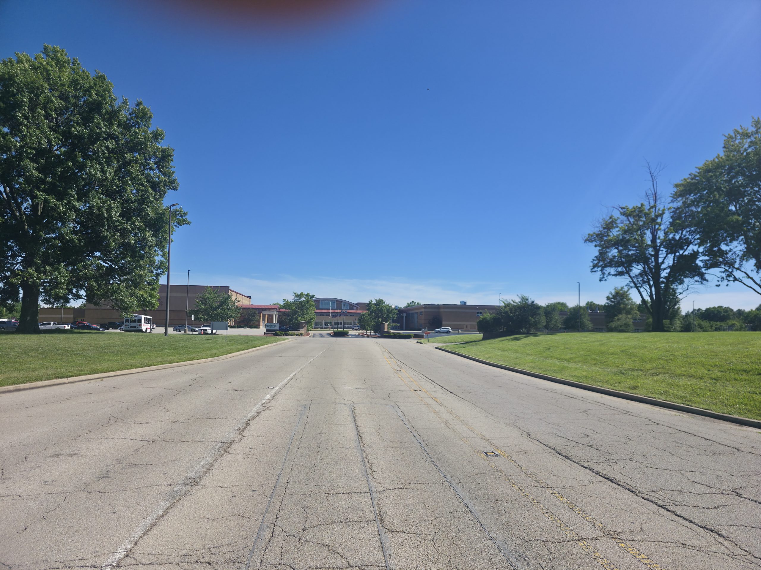 Empty road leading up to a high school, lined with trees under a clear blue sky
