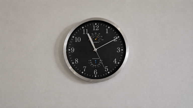Round wall clock with a black face and brushed-metal rim, small thermometer and hygrometer dials inside