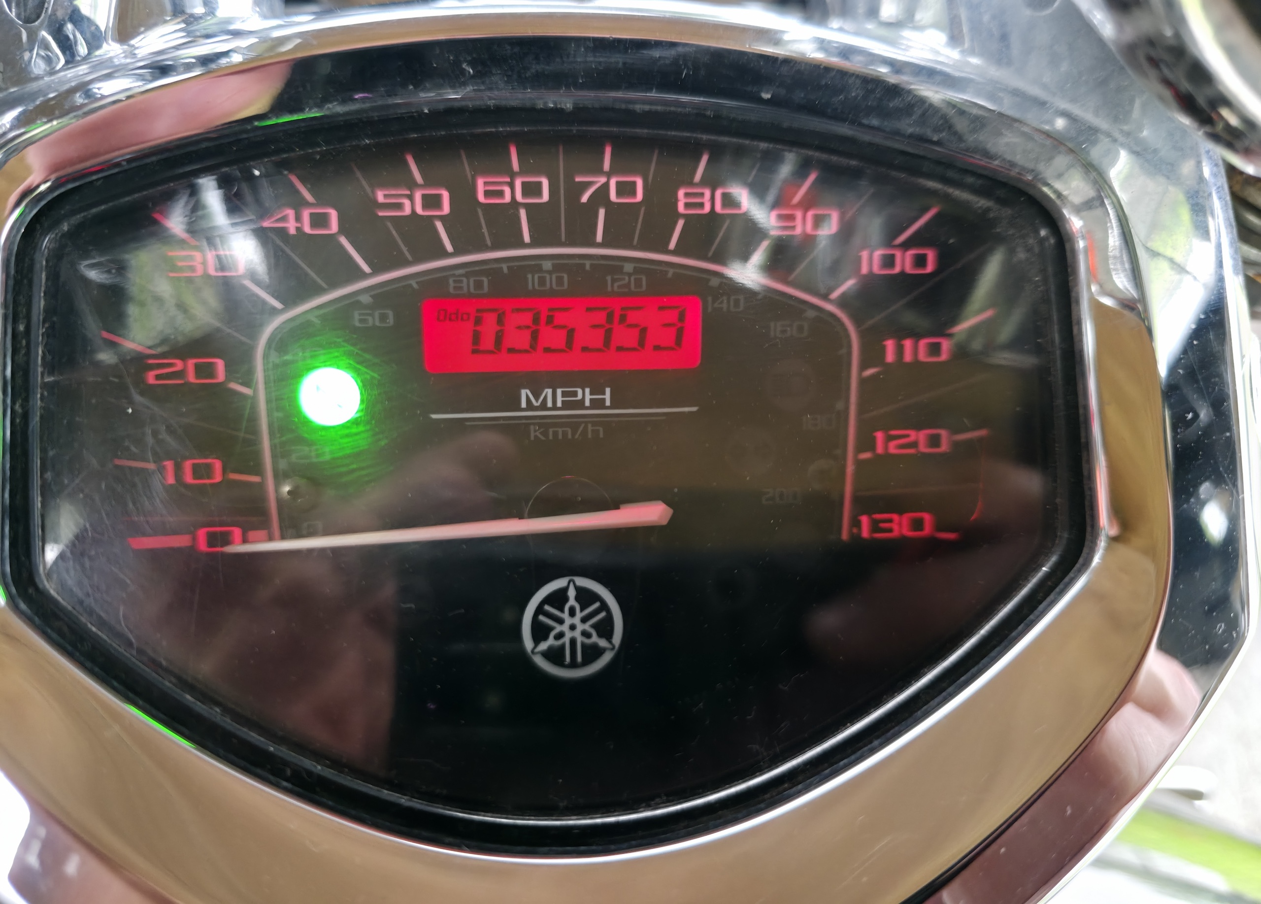 Close-up of a motorcycle odometer reading 035353 miles, speedometer glowing in low light