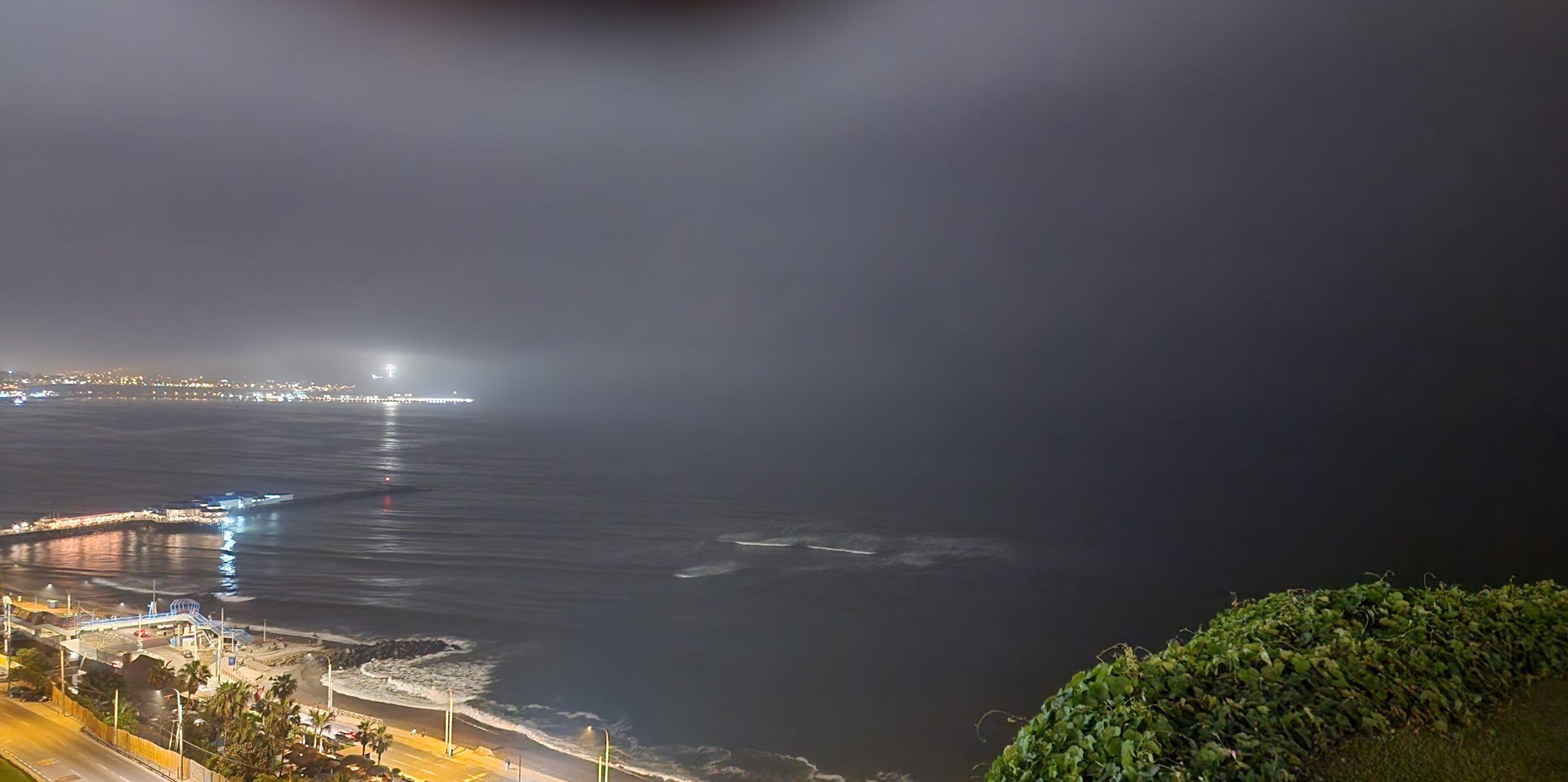 Fog rolling over a dark coastline at night, distant city lights barely visible across the water