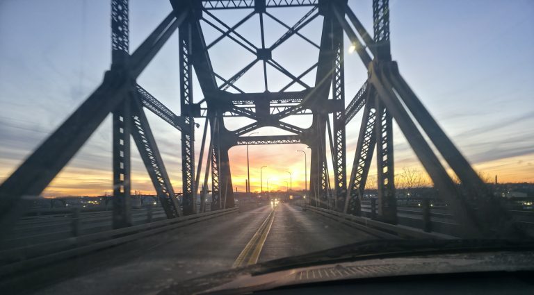 View through a steel truss bridge at sunrise on the ride, empty road ahead and the sun low on the horizon