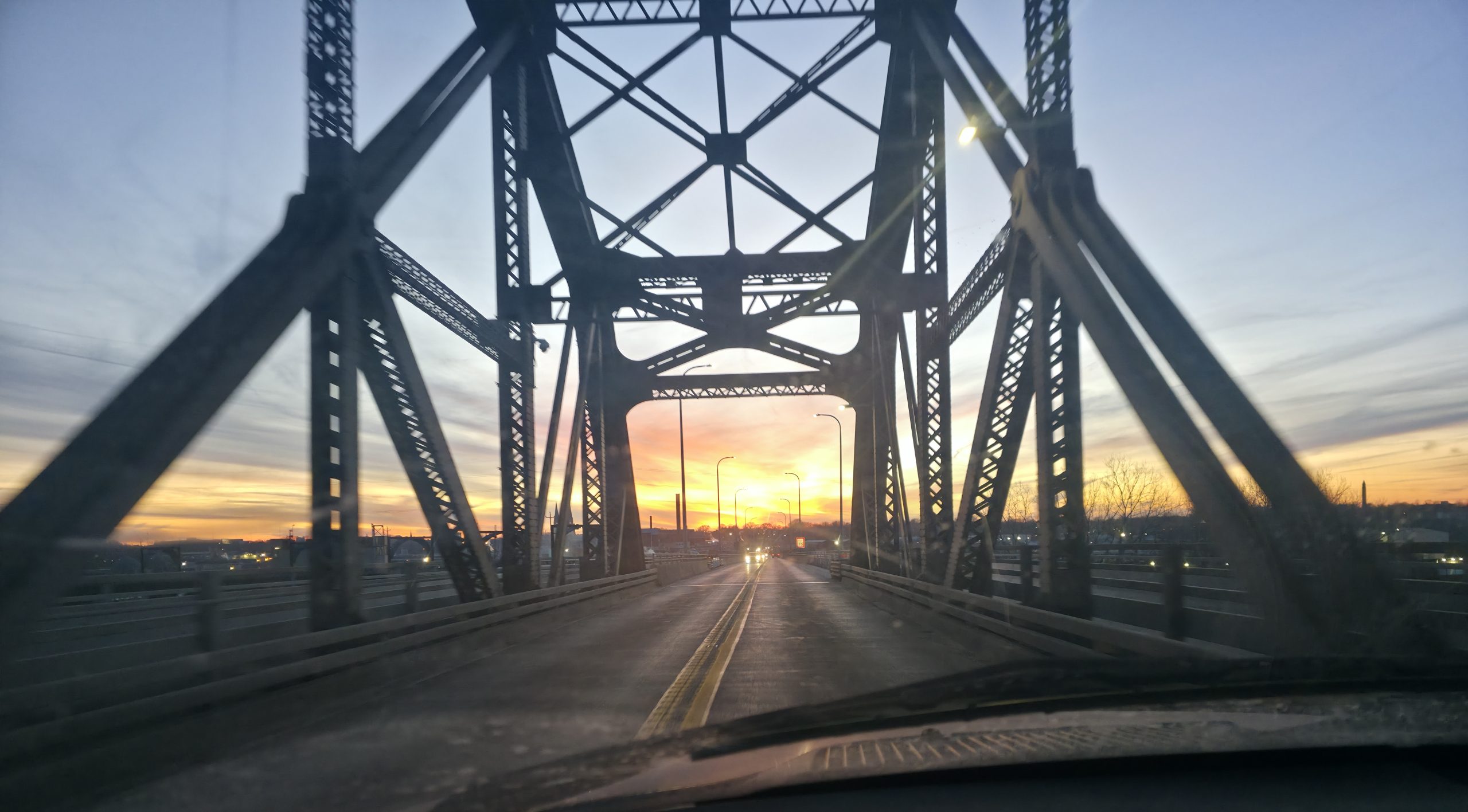 View through a steel truss bridge at sunrise on the ride, empty road ahead and the sun low on the horizon