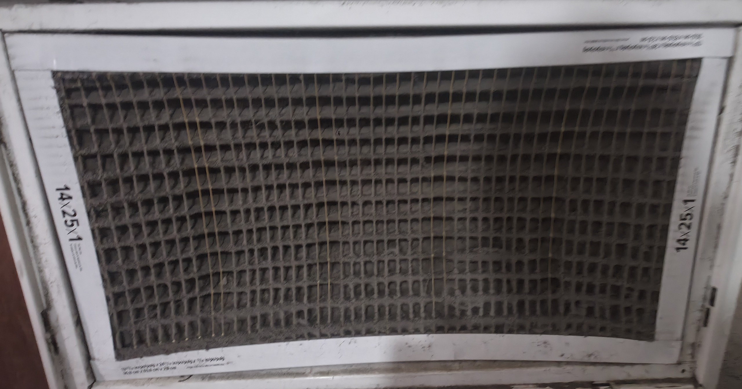 Clogged, dust-caked HVAC air filter labeled 14x25x1 in a white return housing, overdue for replacement