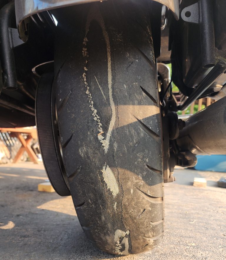 Close-up of a worn rear motorcycle tire with the fabric cords showing through the tread.